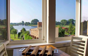 A room with a large window overlooking a lake, a brick wall, and a table with rolled-up items. - 2 bedroom lovely apartment in Röbel (Röbel)