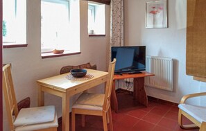 A small room with a wooden table, two chairs, a television on a stand, a radiator, and a window with a curtain. - Cozy apartment in Röbel with lake view (Röbel)
