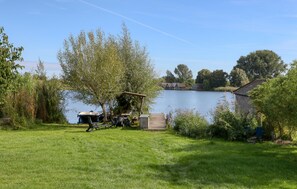 A lakeside property with a grassy lawn, a dock with boats, and a small wooden building. - Cozy apartment in Röbel with lake view (Röbel)