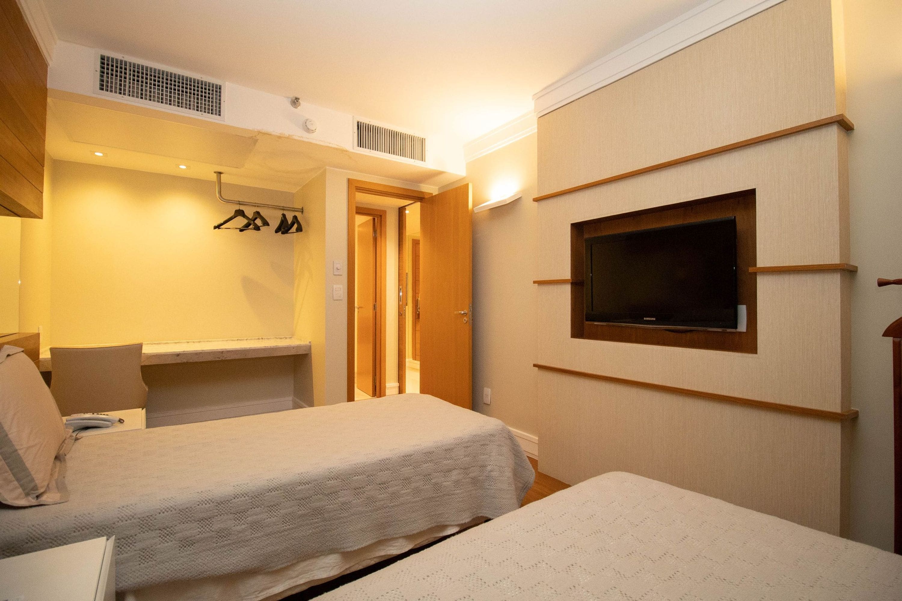 Habitación de hotel con dos camas, un televisor montado en la pared y un perchero.