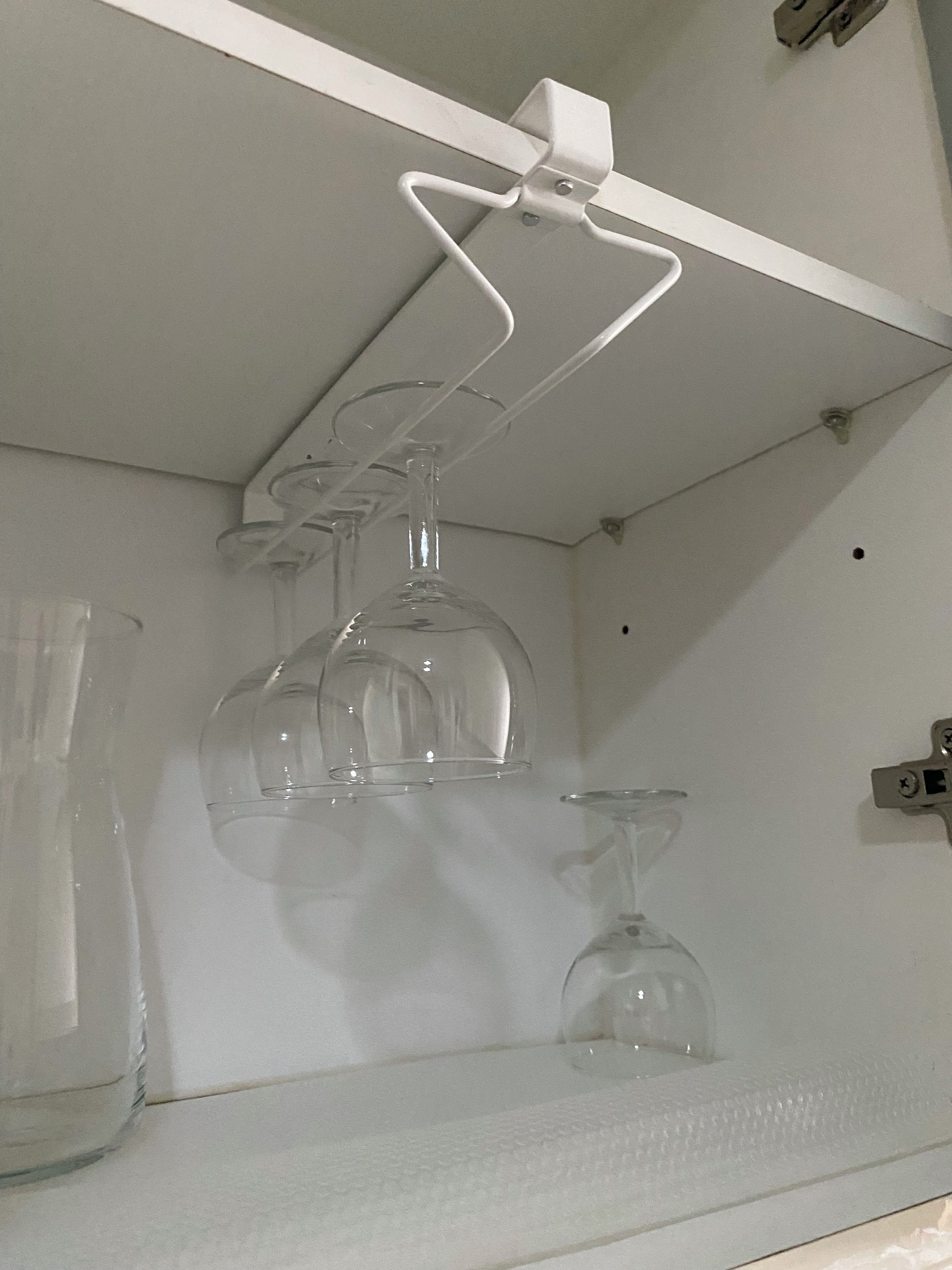 Une étagère blanche sur laquelle sont posées trois bouteilles en verre transparent et un verre à vin.