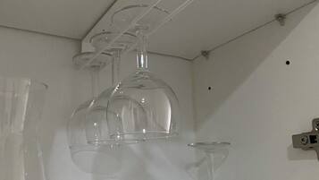 Une étagère blanche sur laquelle sont posées trois bouteilles en verre transparent et un verre à vin.