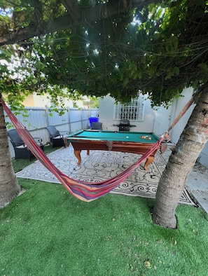 Ein Billardtisch mit Hängematte und einem gemusterten Teppich im Garten.