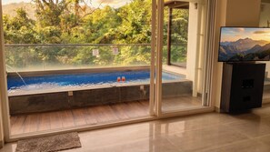 A room with a glass door leading to a pool, a television, and a view of a mountainous landscape. - Luxurious 3-bedroom apartment villa with private pool in tranquil Candolim (Candolim)