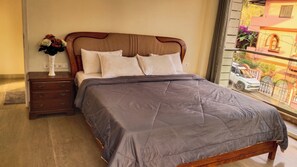 A bed with a headboard, a bedside table with a vase of flowers, and a view of a street through a window. - Luxurious 3-bedroom apartment villa with private pool in tranquil Candolim (Candolim)