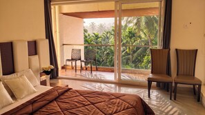 A hotel room with a bed, a chair, a balcony with a view of palm trees, and a window. - Luxurious 3-bedroom apartment villa with private pool in tranquil Candolim (Candolim)