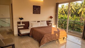 A bedroom with a bed, bedside tables, a chair, and a window with a view of palm trees. - Luxurious 3-bedroom apartment villa with private pool in tranquil Candolim (Candolim)
