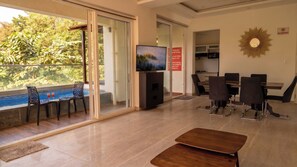 Un salon moderne avec vue sur la piscine, un téléviseur à écran plat et un coin repas comprenant des chaises et une table.