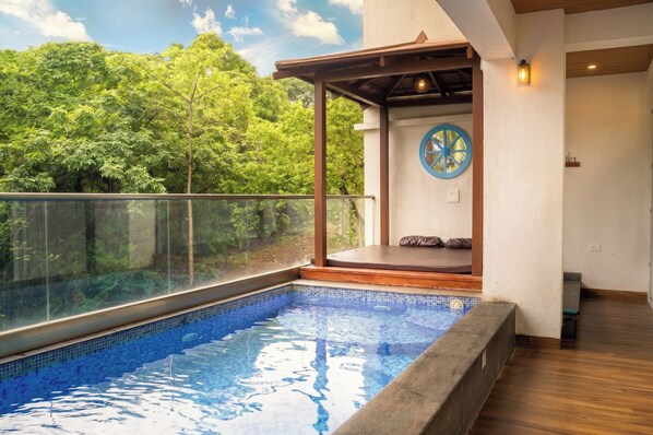 Une piscine dotée d’une paroi en verre, d’une terrasse en bois et offrant une vue sur une végétation luxuriante.