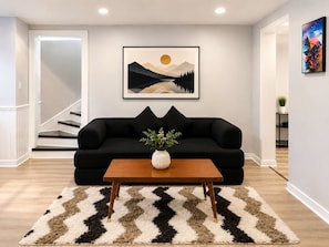 A living room with a black sofa, a wooden coffee table, and a framed landscape painting on the wall.