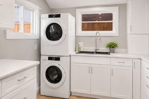 A laundry room with stacked washer and dryer, a sink, cabinets, and a window.