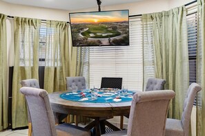 A room with a round table set for a game, a television mounted on the wall, and curtains on the windows. - Resort-Style Retreat: Pool • Spa • Game Room (Scottsdale)