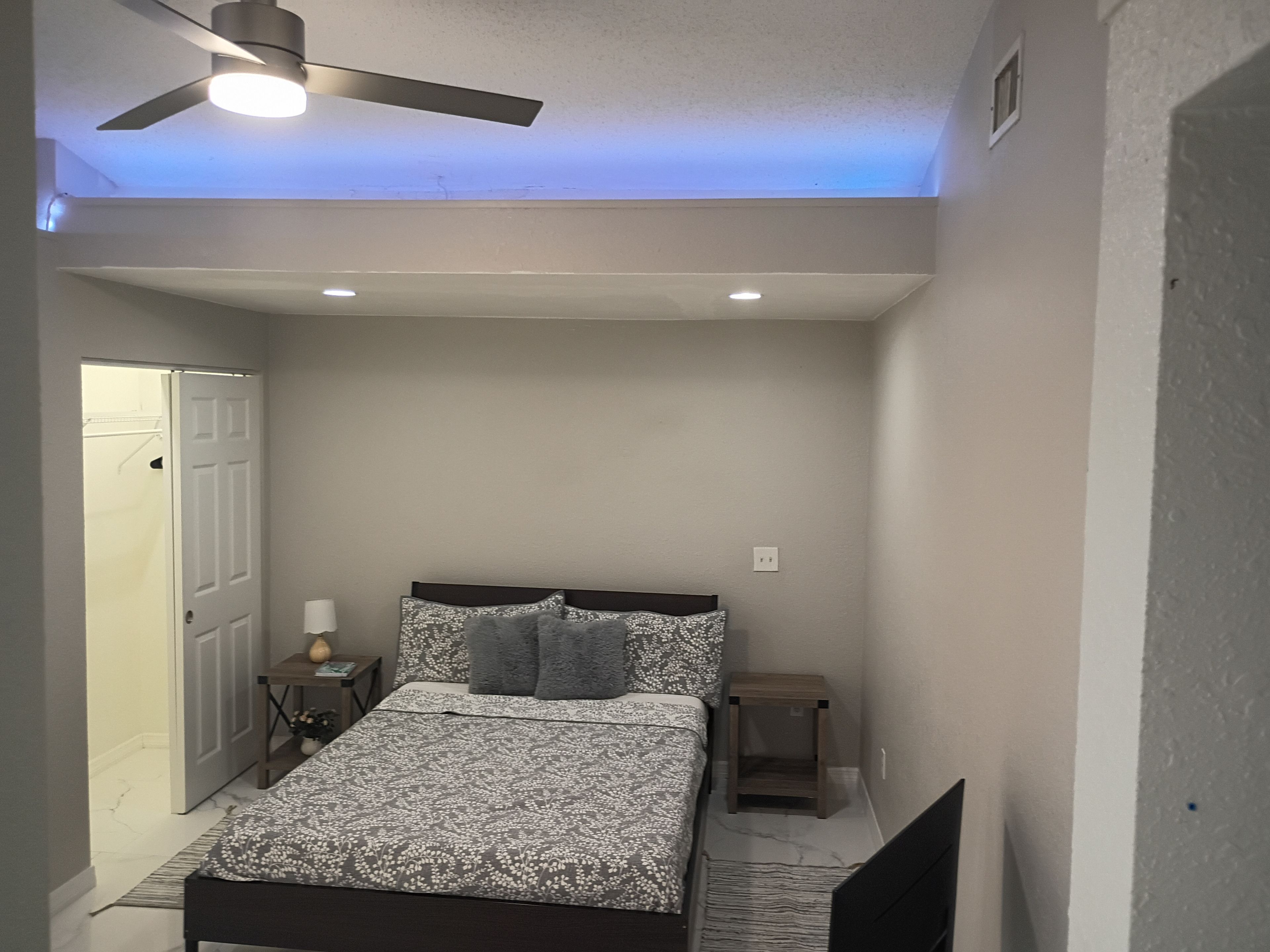 A bedroom with a bed, a ceiling fan, a nightstand, and a door.