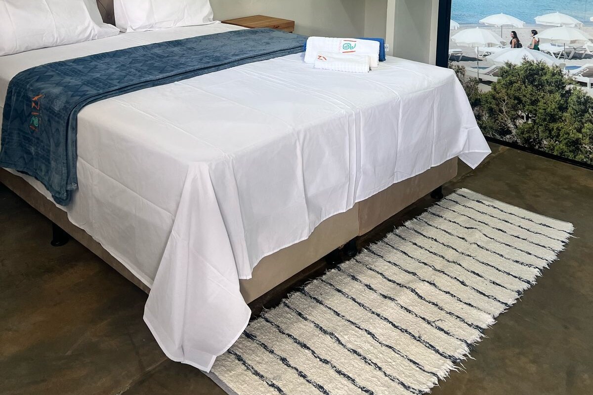 Een slaapkamer met een bed, een groot raam met uitzicht op zee en een schilderij aan de muur.