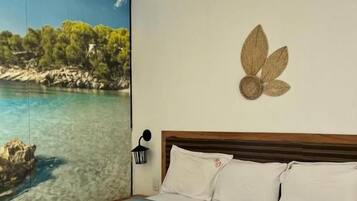 A hotel room with a large window offering a scenic view of a coastal landscape, a bed with white linens, and a decorative wall piece.