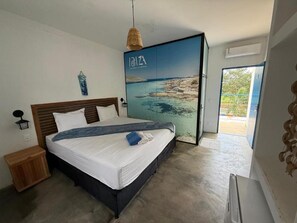 Een slaapkamer met een bed, een nachtkastje, een wandlamp en uitzicht op zee door een glazen deur.