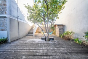 Eine Holzterrasse mit einem Baum, einem kleinen Schuppen und einer Treppe, die zu einem Gebäude führt.