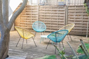 Eine Holzterrasse mit drei Korbstühlen und einem Tisch.