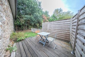 A wooden deck with a table and chairs, surrounded by a wooden fence and a stone wall. - Appartement Cosy au coeur de la nature (Riec-sur-Bélon)