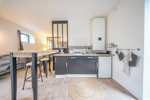 Cocina compacta con una isla central, taburetes de bar, un refrigerador y un colgador para ollas.