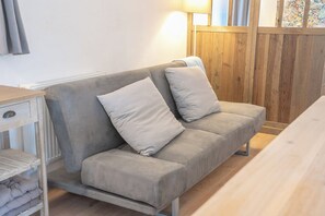 Un sofá de tonos neutros con dos cojines, una mesa de madera y un radiador en una habitación con paneles de madera.