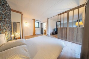 A bedroom with a large bed, a mirror, a television, and a wooden partition. - Appartement Cosy au coeur de la nature (Riec-sur-Bélon)