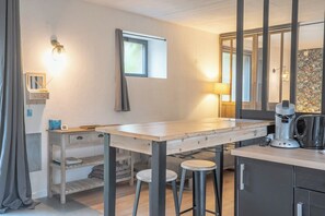 Una cocina compacta con una mesa de madera, dos taburetes, una cafetera y un armario.
