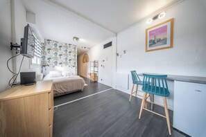 Ein modernes Hotelzimmer mit Bett, Schreibtisch, Stuhl, Fernseher und einem Bild an der Wand.