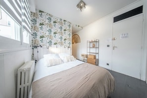 A bedroom with a bed, a radiator, a shelf with decorative items, and a door. - Nid Douillet Cœur de ville (Lorient)