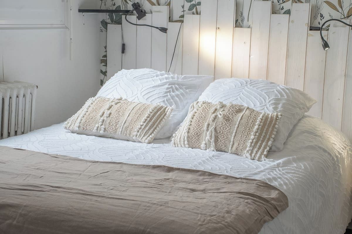 A bed with a white quilt and two pillows, a radiator, and a wooden headboard with a plant.