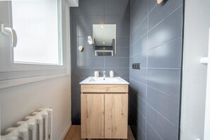 Ett badrum med ett vitt handfat, träskåp, en spegel och ett element.