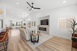 A spacious living area with a sofa, dining table, and a television. - Golden Hour 1 story 4 BR 3-car garage GATED (Las Vegas)