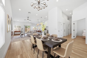 A spacious dining area with a dark wooden table, beige chairs, and a modern chandelier. - Golden Hour 1 story 4 BR 3-car garage GATED (Las Vegas)