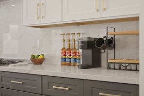 A kitchen with white cabinets, a coffee machine, and a fruit bowl. - Golden Hour 1 story 4 BR 3-car garage GATED (Las Vegas)