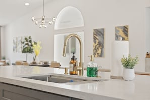 A modern kitchen with a stainless steel sink, a gold faucet, and a green soap dispenser. - Golden Hour 1 story 4 BR 3-car garage GATED (Las Vegas)
