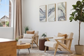 A modern living room with a large window, two armchairs, a round coffee table, and a potted plant. - Golden Hour 1 story 4 BR 3-car garage GATED (Las Vegas)