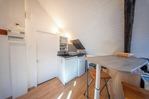 A compact kitchen with a built-in oven, a small refrigerator, and a countertop with stools. - Studio au Cœur du centre historique (Quimper)