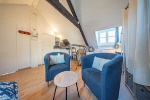 A cozy loft-style room with a sloped ceiling, two blue armchairs, a small round table, and a kitchenette in the background. - Studio au Cœur du centre historique (Quimper)