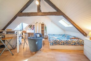 A loft bedroom with a sloped ceiling, a bed with a floral bedspread, a desk with a chair, and a small table. - Studio au Cœur du centre historique (Quimper)