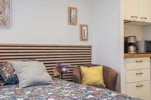 A hotel room with a bed, a chair, a small table with a vase of flowers, and a kitchenette area. - Le pied-à-terre idéal au centre (Quimper)