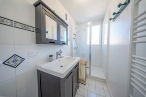 Un baño con lavamanos blanco, muebles oscuros, un espejo y zona de ducha.