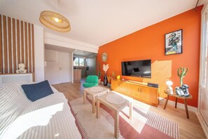 Una sala moderna con un sofá, una televisión, un comedor y una cocina al fondo.