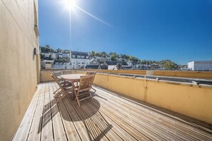 Una terraza de madera con una mesa y sillas, con vistas a una zona residencial con casas y árboles.