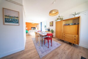 Un comedor con una mesa y sillas de madera, una silla roja, un aparador de madera con plantas y un cuadro en la pared.