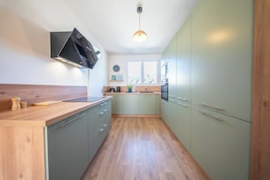 Eine moderne Küche mit einer Holzausziehtafel, grünen Schränken und einer schwarzen Dunstabzugshaube.