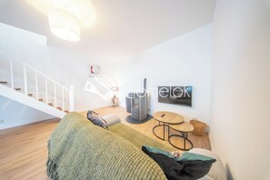 A modern living room with a sofa, a TV, a fireplace, and a staircase. - Charmant Duplex avec poêle - 10 min Gare (Lorient)
