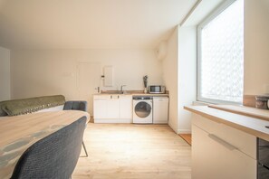 A compact kitchen with a washing machine, a microwave, and a dining area with a table and chairs. - Charmant Duplex avec poêle - 10 min Gare (Lorient)