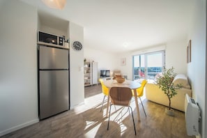 A modern kitchen with a built-in microwave, a refrigerator, and a dining area with a table and chairs. - T2 neuf & lumineux Calme et plages à 5 min (Guidel)