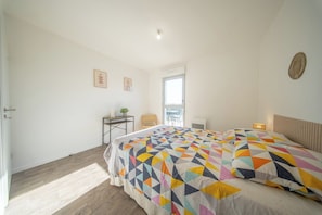 A bedroom with a bed, a desk, a chair, and a window. - T2 neuf & lumineux Calme et plages à 5 min (Guidel)