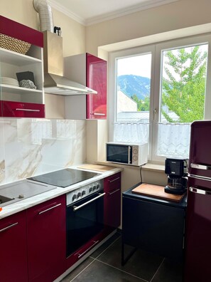 A compact kitchen with a stove, microwave, and coffee maker. - Kaiserplatz Suite in a Prime Location (Bad Reichenhall)